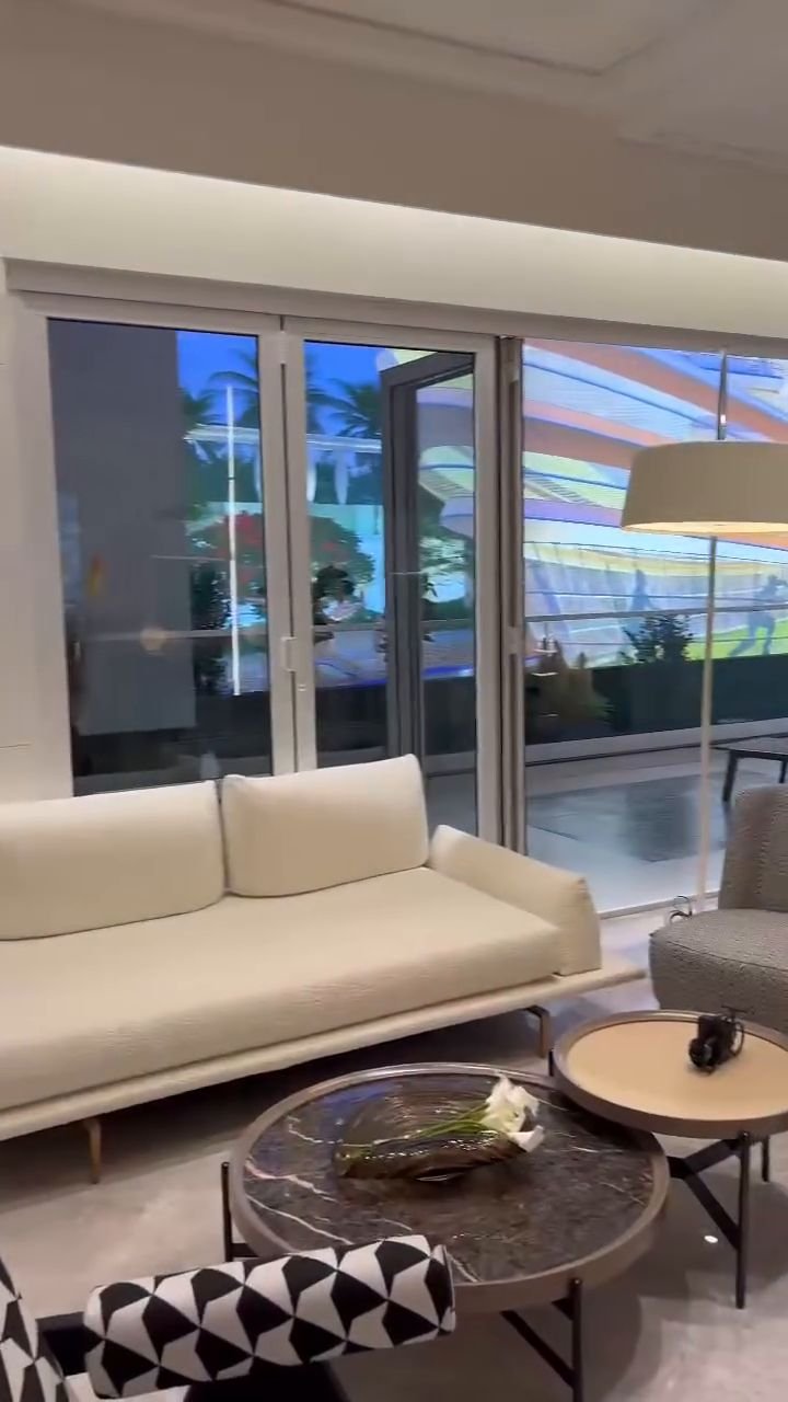 Still from the walkthrough film: a furnished living area with a sofa beside sliding glass doors.